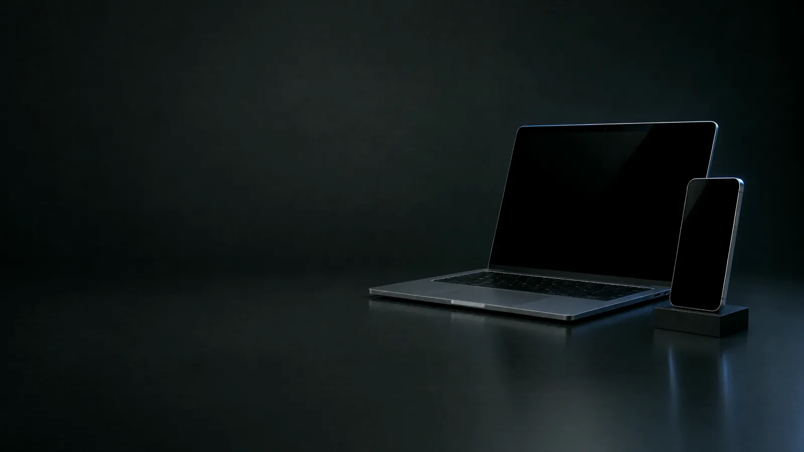 A laptop and a phone standing on a dark desk, edged in blue light